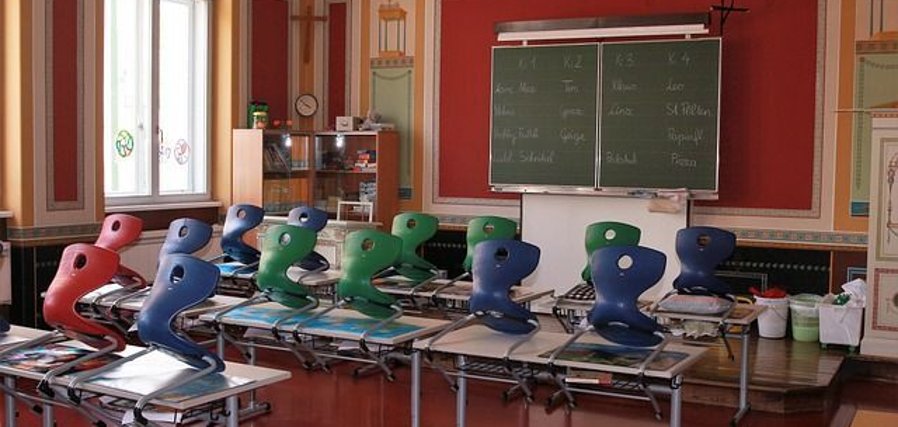 Klassenzimmer mit hochgestellten Stühlen und Blick auf die Tafel
